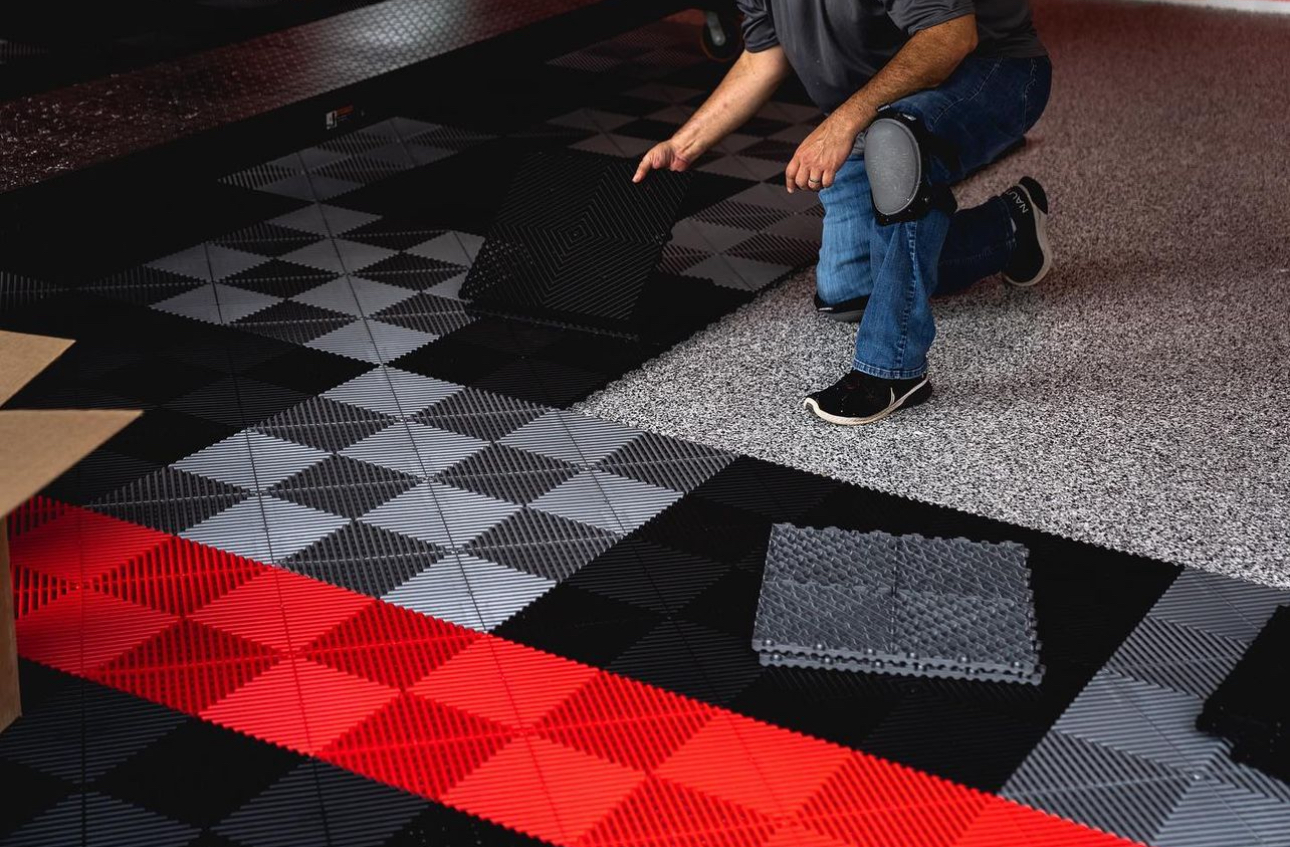 Installer kneeling to snap a black tile into a black, grey and red diamond-pattern garage floor